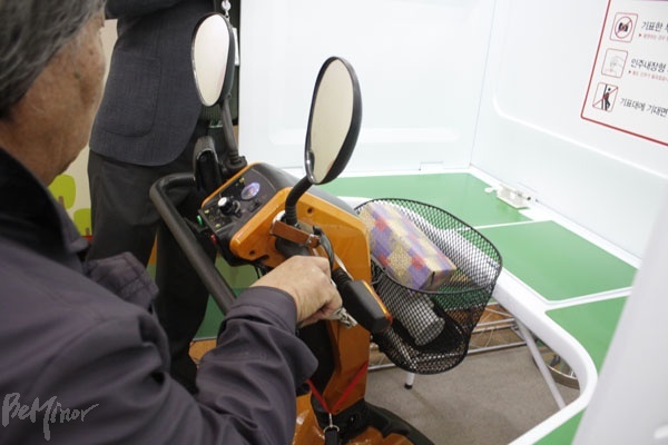 낮은 기표대에 걸리는 전동스쿠터. 전동스쿠터 사용자는 기표대에 손이 닿지 않아 타인의 보조를 받아야 한다.