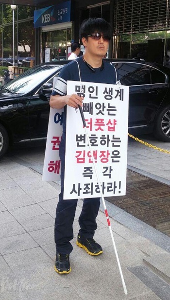 한 시각장애인이 더풋샵을 변호하는 김앤장 규탄 피켓 시위를 벌이고 있다.