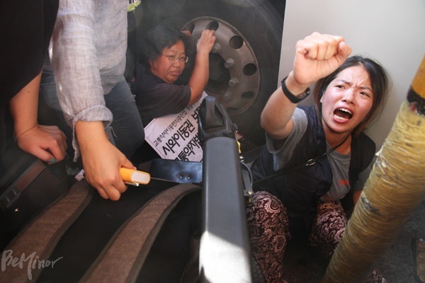 장애인 활동가가 장애인의 시외이동권 보장을 촉구하며 휠체어에서 내려와 두 손으로 버스 앞바퀴를 꼭 잡고 있다.   