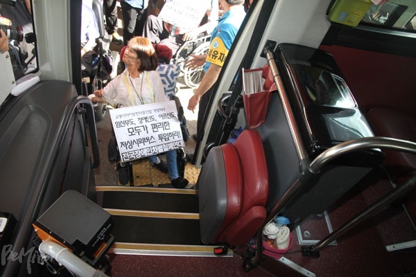 휠체어를 탄 채 오를 수 없는 버스 문 앞에 휠체어 탄 장애인이 서 있다. 