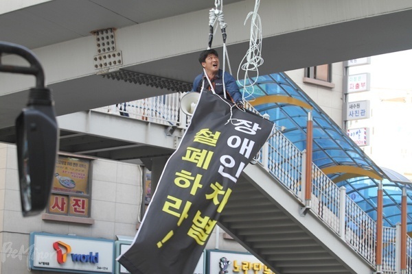 지난 6월 2일 이도건 경기420공투단 집행위원장이 수원역 앞 육교에 매달려 경기도 장애인 이동권 보장을 촉구하는 모습.