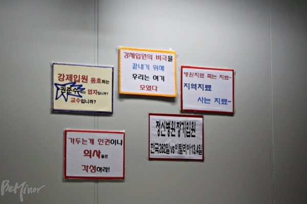 기자회견이 진행된 인권위 배움터 한쪽 벽에 '강제입원 옹호하는 권준수 씨는 업자입니까 교수입니까?', '병원치료 죽는 치료, 지역치료 사는 치료', '가두는 게 인권이냐 의사들은 각성하라!' 등의 문구가 붙어 있다. 