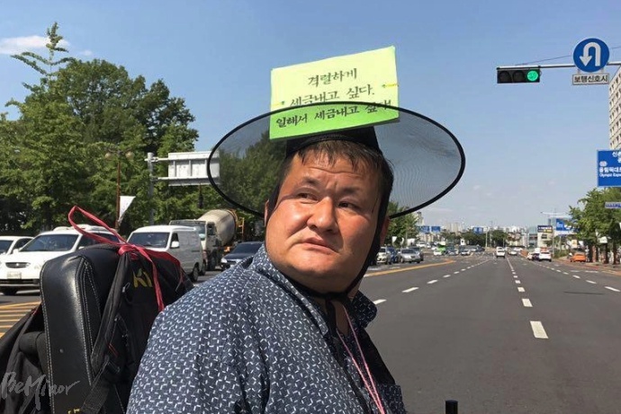 한 기자회견 참가자가 "격렬하게 세금내고 싶다. 일해서 세금내고 싶다!"라는 문구가 적힌 갓을 쓰고 있는 모습.