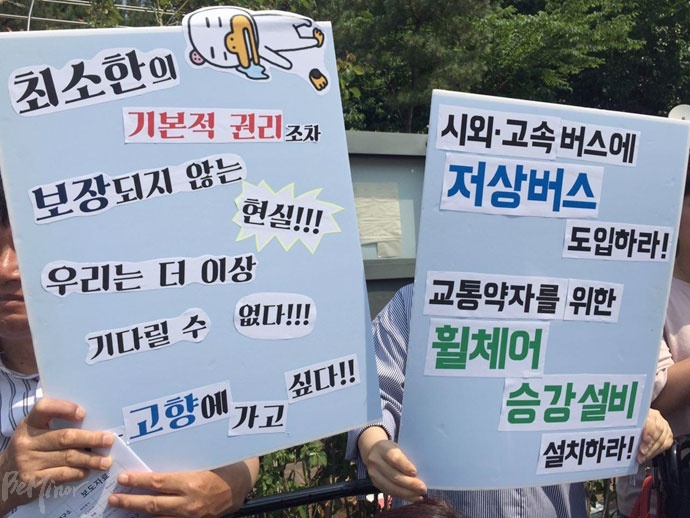 "최소한의 기본적 권리조차 보장되지 않는 현실, 우리는 더이상 기다릴 수 없다!", "시외·고속버스에 저상버스 도입하라. 교통약자를 위한 휠체어 승강설비 설치하라!" 피켓을 들고 있는 사람들. 