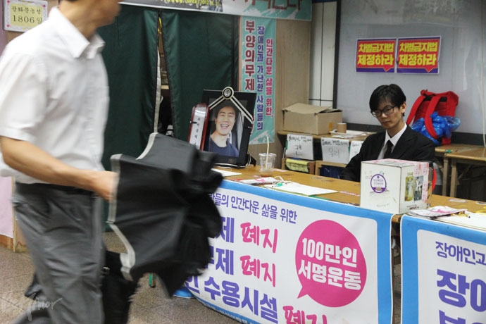 장애등급제·부양의무제폐지 농성장에 영정으로 돌아온 고 박종필 감독. 그 곁에 송윤혁 감독이 함께 앉아있다. 장애등급제·부양의무제폐지 농성장에 영정으로 돌아온 고 박종필 감독. 그 곁에 송윤혁 감독이 함께 앉아있다.