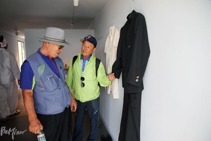 김춘근 씨(사진 오른쪽)가 선감역사발물관에 전시된 옛 원생 동복을 매만지며 동료와 대화를 나누고 있다.