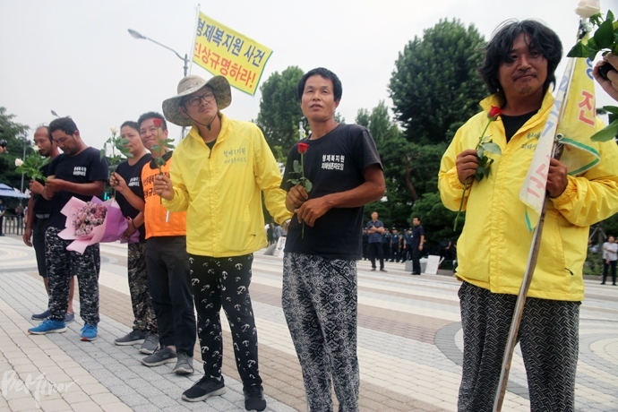 국토대장정을 마친 형제복지원 피해생존자들이 꽃을 선물받고 환하게 웃고 있다.