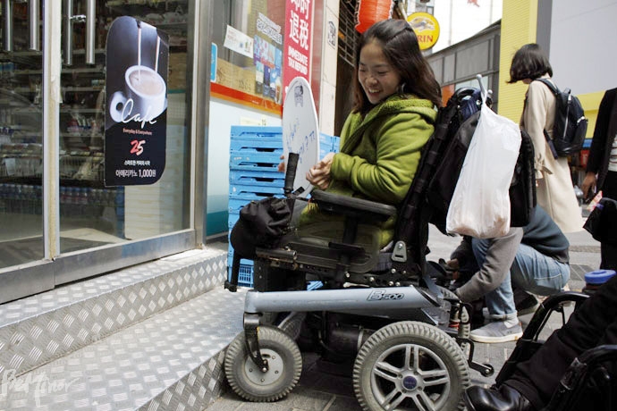 휠체어 탄 장애인이 1층 편의점에 들어가려고 하나 턱 때문에 갈 수 없는 상황을 직접 보여주고 있다. 