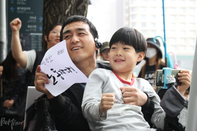 장애인노동자대회에 자녀와 함께온 참석자가 집회 중 웃고 있는 모습. 장애인노동자대회에 자녀와 함께온 참석자가 집회 중 웃고 있는 모습.
