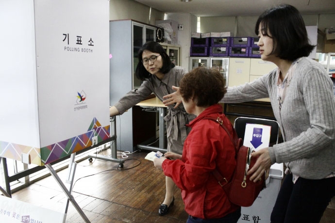 발달장애인 유권자가 선관위 직원 안내에 따라 투표용지를 받고 기표장에 들어가고 있다.