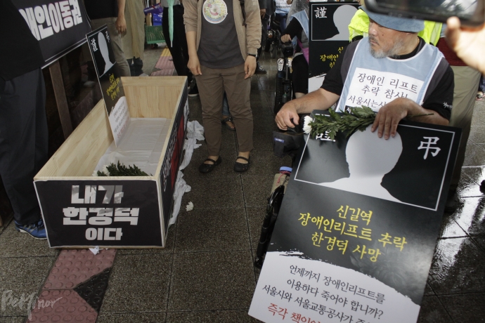 지하철에 탑승하기 전 사람들이 '내가 한경덕이다'라고 쓰인 관에 헌화를 하고 있다.