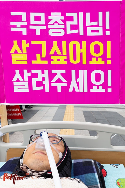침대에 누워있는 근육장애인 머리맡에 “국무총리님 살고 싶어요. 살려주세요”라는 피켓이 걸려있다.