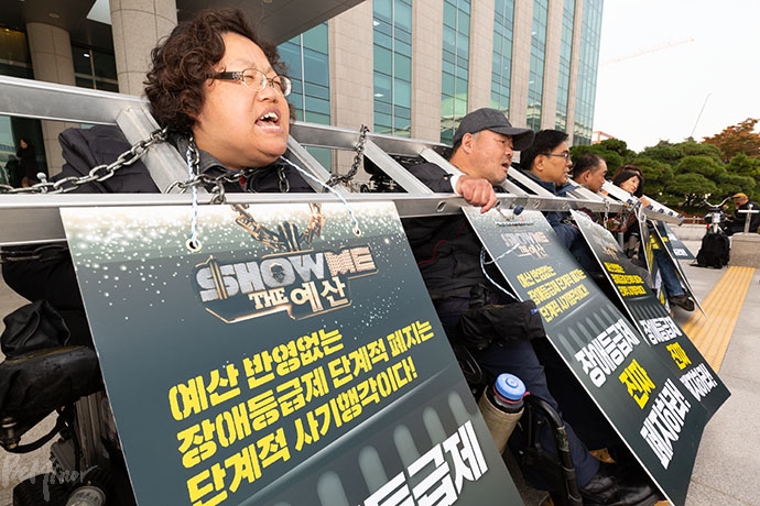 전국장애인차별철폐연대 소속 장애인활동가 30여 명은 5일 낮 12시, 국회의원회관 앞에서 사다리와 쇠사슬을 목에 걸고 “예산 없는 장애등급제 단계적 폐지는 사기”라며 국회에 내년도 장애인 복지 예산 확대를 촉구했다. 