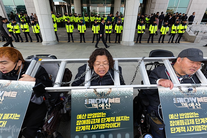 사다리와 쇠사슬을 목에 걸고선 내년도 장애인 복지 예산 확대를 촉구하는 장애인 활동가들 뒤로 경찰이 지키고 서있다. 