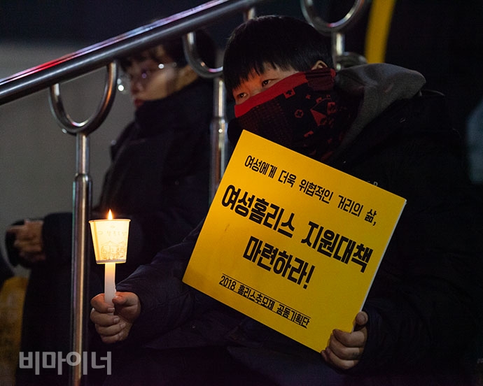 머리를 짧게 자른 여성 홈리스가 추모문화제에 참석해 발언을 듣고 있는 모습. 그의 손에는 ‘여성홈리스 지원대책 마련하라!’는 손팻말이 들려있다.