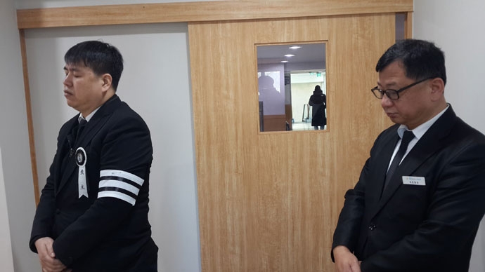 무연고 사망자 장례 중 기도를 드리고 있는 의전팀장과 대리상주. 빈소 출입문 작은 창밖으로 보이는 아들의 뒷모습 무연고 사망자 장례 중 기도를 드리고 있는 의전팀장과 대리상주. 빈소 출입문 작은 창밖으로 보이는 아들의 뒷모습