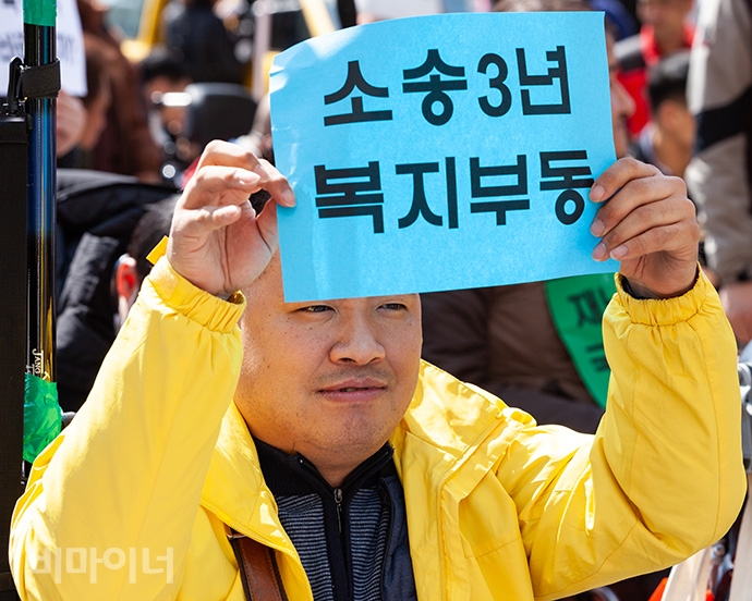 한 참여자가 메르스로 촉발된 장애인 재난 감염 관련 소송이 3년째 진행 중임에도 재판에 불참하는 등 무책임한 태도로 일관하는 복지부를 비판하는 내용이 담긴 손피켓 “소송 3년 복지부동”을 들고 있다. 사진 박승원.