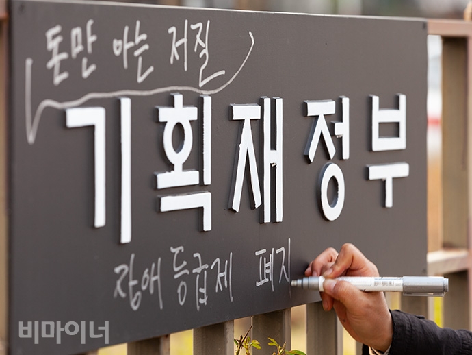 420공투단 회원이 정부세종청사 기획재정부 명판에 '돈만 아는 저질, 장애등급제 폐지'라는 문구를 덧붙여 써넣고 있다. 사진 박승원 