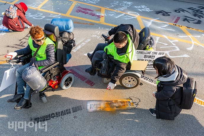 장애인활동가들이 기획재정부 건물 앞 도로에 ‘장애등급제 폐지’, ‘장애인수용시설 폐지’, ‘부양의무제 완전 폐지하라’ 등의 문구를 스프레이 라카로 새기고 있다. 사진 박승원