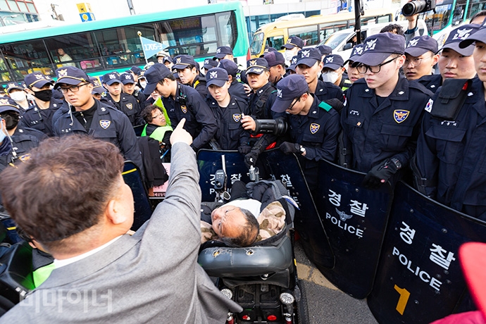 경기420공투단 활동가들이 수원역 광장 교차로를 점거하려고 하자 경찰들이 방패로 막아서고 있다. 회색 정장을 입은 경찰이 장애인 활동가들을 향해 손가락질하며 고함치고 있다. 사진 박승원