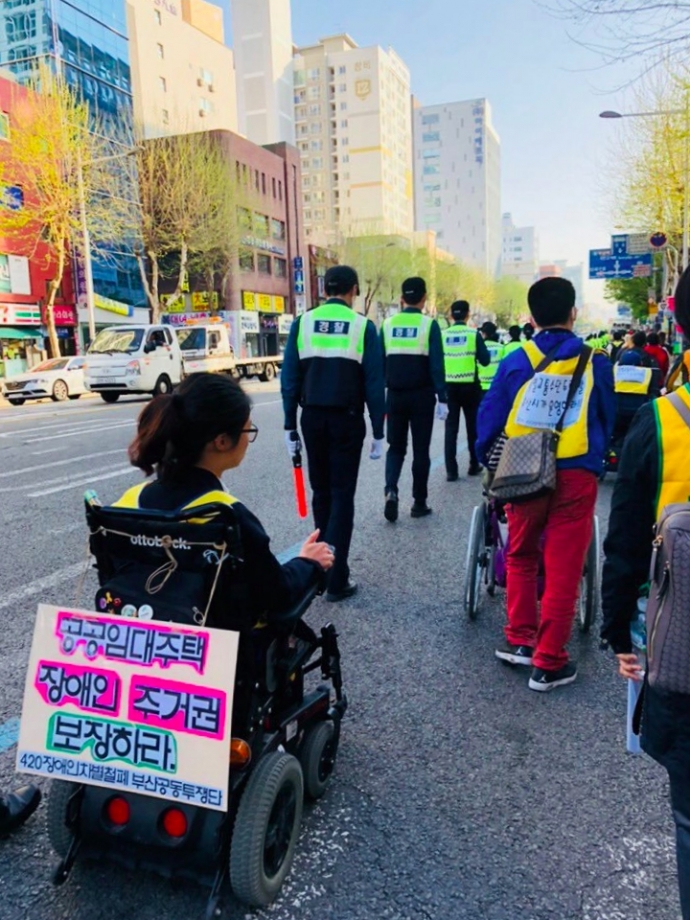 한 장애여성이 휠체어 뒤에 '공공임대주택 장애인 주거권 보장하라'는 문구가 적힌 피켓을 달고 집회에 참여한 모습. 사진제공 부산장애인차별철폐연대