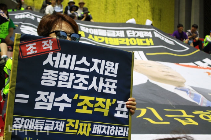 전국장애인차별철폐연대는 4일 오전 11시 세종문화회관 앞에서 ‘장애등급제 진짜 폐지 예산 확보! 홍남기 기획재정부 장관 찾아 삼만리 농성 선포 기자회견’을 열고 장애계가 요구하는 ‘진짜 폐지’를 위해 7월 1일까지 28일간 이 자리에서 농성할 것이라고 밝혔다. 기자회견 참가자가 “서비스지원 종합조사표=점수 조작표”라고 적힌 손피켓을 들고 있다. 사진 강혜민