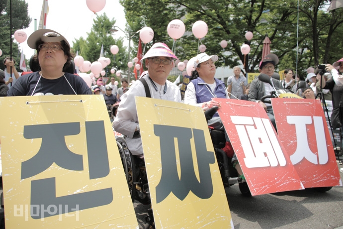 장애등급제 ‘진짜’ 폐지를 위한 투쟁 선포식에서 ‘진짜 폐지’ 플래카드를 목에 걸고 있는 참가자 모습. 사진 강혜민 장애등급제 ‘진짜’ 폐지를 위한 투쟁 선포식에서 ‘진짜 폐지’ 플래카드를 목에 걸고 있는 참가자 모습. 사진 강혜민