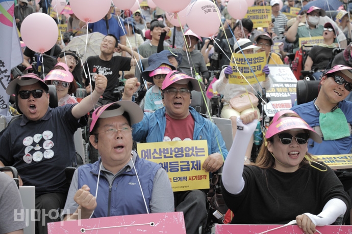 장애등급제 ‘진짜’ 폐지를 위한 투쟁 선포식에서 ‘예산 반영 없는 장애등급제 폐지, 단계적 폐지는 단계적 사기행각’이라는 손팻말을 들고 있는 참가자 모습. 사진 강혜민 장애등급제 ‘진짜’ 폐지를 위한 투쟁 선포식에서 ‘예산 반영 없는 장애등급제 폐지, 단계적 폐지는 단계적 사기행각’이라는 손팻말을 들고 있는 참가자 모습. 사진 강혜민