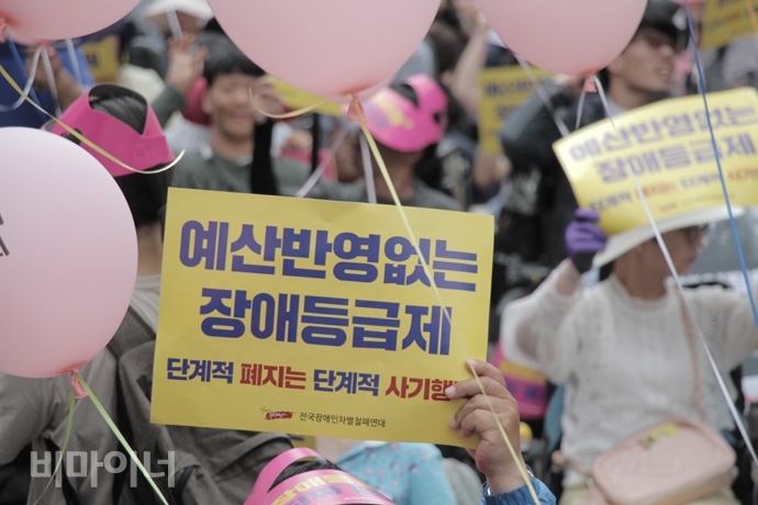 장애등급제 ‘진짜’ 폐지를 위한 투쟁 선포식에서 ‘예산 반영 없는 장애등급제 폐지, 단계적 폐지는 단계적 사기행각’이라는 손팻말을 들고 있는 참가자 모습. 사진 강혜민 장애등급제 ‘진짜’ 폐지를 위한 투쟁 선포식에서 ‘예산 반영 없는 장애등급제 폐지, 단계적 폐지는 단계적 사기행각’이라는 손팻말을 들고 있는 참가자 모습. 사진 강혜민