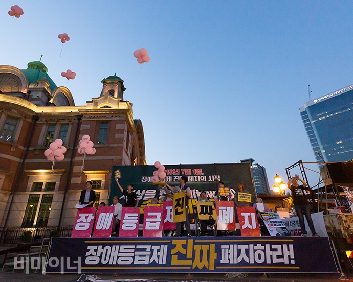 서울역에 모인 집회 참가자들이 ‘장애등급제 진짜 폐지’ 글자가 새겨진 분홍색 풍선을 하늘로 띄어 올리고 있다. 사진 박승원 서울역에 모인 집회 참가자들이 ‘장애등급제 진짜 폐지’ 글자가 새겨진 분홍색 풍선을 하늘로 띄어 올리고 있다. 사진 박승원