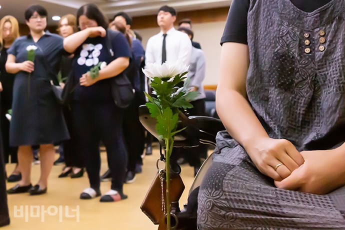 휠체어에 하얀 국화가 꽂혀있다. 뒤로는 눈물 훔치는 사람들이 보인다. 사진 박승원 