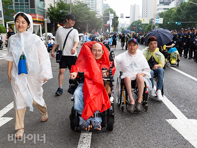 사회보장위원회에서 공덕오거리 방향으로 가는 길에 갑자기 비가 내리기 시작했다. 장애인 활동가들은 미리 준비해온 우산과 우비를 갖추고 행진을 이어갔다. 사진 박승원