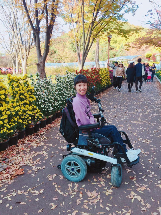 왼쪽에는 꽃이 피어있고 아스팔트 바닥에는 낙엽이 있는 길 위에서 이수나 씨가 환하게 웃고 있다. 사진 제공 대구사람장애인자립생활센터 왼쪽에는 꽃이 피어있고 아스팔트 바닥에는 낙엽이 있는 길 위에서 이수나 씨가 환하게 웃고 있다. 사진 제공 대구사람장애인자립생활센터