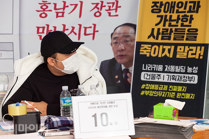 장애계는 기획재정부가 건물주인 인권위 건물에서 31일 기준으로 농성 열흘째를 맞이했다. 농성장을 지키는 활동가 뒤로 “홍남기 장관 만납시다”, “장애인과 가난한 사람들을 죽이지 말라”는 글자가 보인다. 사진 박승원