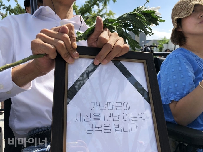 지난 8월, 관악구에서 일어난 북한이탈주민 모자 사망에 대한 추모제에 참가한 사람이 “가난 때문에 세상을 떠난 이들의 명복을 빕니다”라고 적힌 액자와 국화를 들고 있다. 사진 강혜민 지난 8월, 관악구에서 일어난 북한이탈주민 모자 사망에 대한 추모제에 참가한 사람이 “가난 때문에 세상을 떠난 이들의 명복을 빕니다”라고 적힌 액자와 국화를 들고 있다. 사진 강혜민