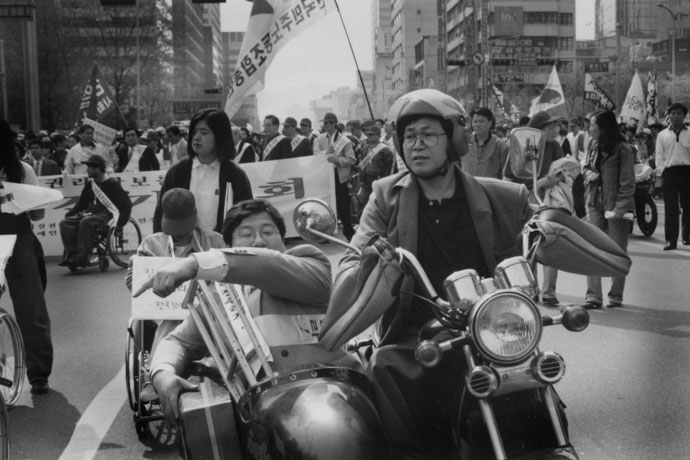 1996년 장애인고용촉진걷기대회에서 정태수 열사(왼쪽)와 박흥수 열사(오른쪽). 박흥수 열사가 자신의 삼륜오토바이를 운전하고 있다. 사진 정태수열사추모사업회