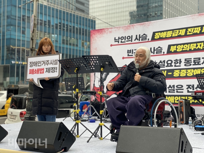 박경석 전국장애인야학협의회 이사장이 발언을 하고 있고 조아라 장애인와인권발바닥행동 활동가가 ‘장애인거주시설 폐쇄법 제정!’이라고 적혀 있는 피켓을 들고 있다. 사진 이가연 박경석 전국장애인야학협의회 이사장이 발언을 하고 있고 조아라 장애인와인권발바닥행동 활동가가 ‘장애인거주시설 폐쇄법 제정!’이라고 적혀 있는 피켓을 들고 있다. 사진 이가연
