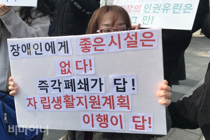 서울장애인차별철폐연대 등 9개 장애단체는 17일 오후 3시. 금천구청 앞에서 기자회견을 열고, 금천구의 신속한 행정처분 이행을 요구하고 나섰다. 기자회견 참가자가 ‘장애인에게 좋은 시설은 없다! 즉각 폐쇄가 답! 자립생활지원계획 이행이 답!’이라는 손팻말을 들고 있다. 사진 허현덕