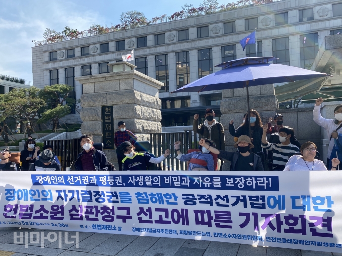 헌법재판소는 27일, 재판관 6:3의 의견으로 신체에 장애가 있는 선거인에 대해 투표보조인이 가족이 아닌 경우 반드시 2인을 동반하도록 한 공직선거법 제157조 제6항이 헌법에 위반되지 않는다며 청구를 기각했다. 같은날 장애인차별금지추진연대(아래 장추련) 등은 안국동 헌재 앞에서 장애인의 자기결정권을 침해한 공직선거법 헌법소원 심판청구 선고에 대한 기자회견을 열었다. 사진 이가연