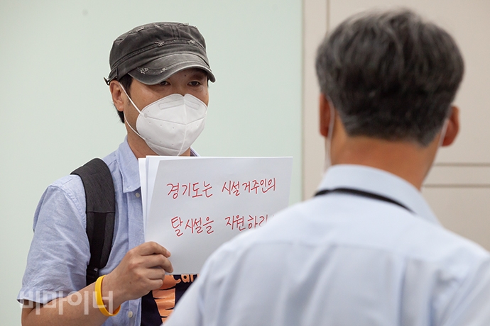 김재환 장애와인권발바닥행동 활동가가 송남영 관장 앞에서 ‘경기도는 시설거주인의 탈시설을 지원하라’라고 적힌 손팻말을 들고 있는 모습. 사진 박승원 