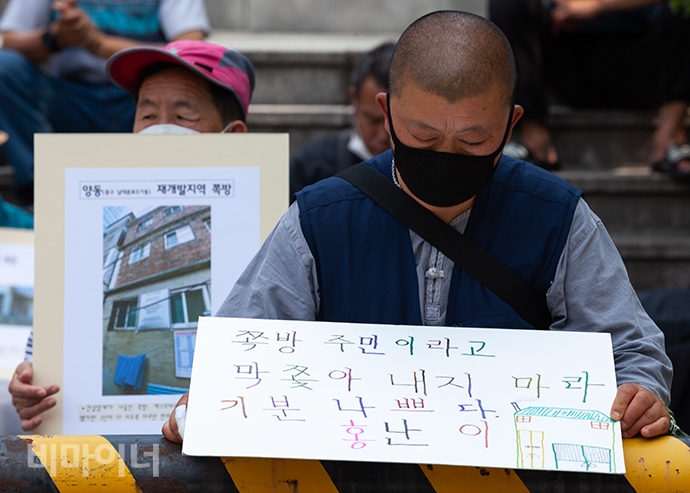 난초(별칭) 씨가 ‘쪽방 주민이라고 막 쫓아내지 마라. 기분 나쁘다’라고 적힌 손팻말을 들여다보고 있다. 사진 박승원