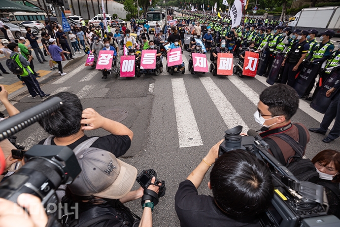 휠체어 이용 활동가들이 ‘장애등급제 폐지’라고 한 글자 한 글자 적힌 손팻말을 목에 걸고 행진을 시작했다. 그 앞에서 기자들이 사진과 영상을  찍는 모습. 사진 박승원