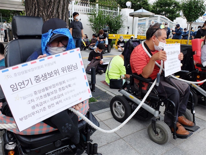 장애인들이 31일 중앙생활보장위원회가 열리는 서울정부청사 앞에서 목에 밧줄을 걸고 2차 기초생활보장종합계획에 생계급여와 의료급여에서 부양의무자 기준 완전 폐지 계획을 담을 것을 촉구하고 있다. 사진 이가연 장애인들이 31일 중앙생활보장위원회가 열리는 서울정부청사 앞에서 목에 밧줄을 걸고 2차 기초생활보장종합계획에 생계급여와 의료급여에서 부양의무자 기준 완전 폐지 계획을 담을 것을 촉구하고 있다. 사진 이가연