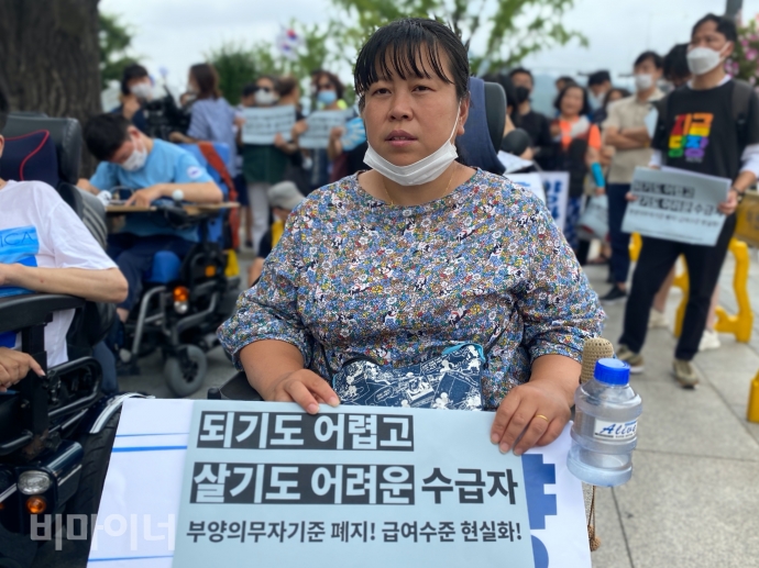 서울 정부종합정사 앞에서 회의결과를 기다리던 한 참가자가 ‘되기도 어렵고 살기도 어려운 수급자, 부양의무자기준 폐지! 급여수준 현실화!’라고 적힌 피켓을 들고 있다. 사진 이가연 서울 정부종합정사 앞에서 회의결과를 기다리던 한 참가자가 ‘되기도 어렵고 살기도 어려운 수급자, 부양의무자기준 폐지! 급여수준 현실화!’라고 적힌 피켓을 들고 있다. 사진 이가연