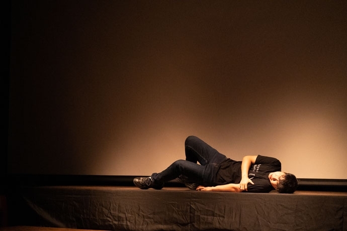 커다란 빔프로젝터 스크린을 배경으로 낮게 올라온 검은색 단상 위를 비추는 조명에 누운 희제. 엉덩이가 바닥에 닿지 않게 하려는 듯 양쪽 다리를 굽혀서 무릎을 올린 상태로, 인상을 쓰며 오른손으로 왼쪽 팔뚝을 잡고 있다. 연극 「아파도 미안하지 않습니다」의 한 장면. 사진 김덕중 커다란 빔프로젝터 스크린을 배경으로 낮게 올라온 검은색 단상 위를 비추는 조명에 누운 희제. 엉덩이가 바닥에 닿지 않게 하려는 듯 양쪽 다리를 굽혀서 무릎을 올린 상태로, 인상을 쓰며 오른손으로 왼쪽 팔뚝을 잡고 있다. 연극 「아파도 미안하지 않습니다」의 한 장면. 사진 김덕중