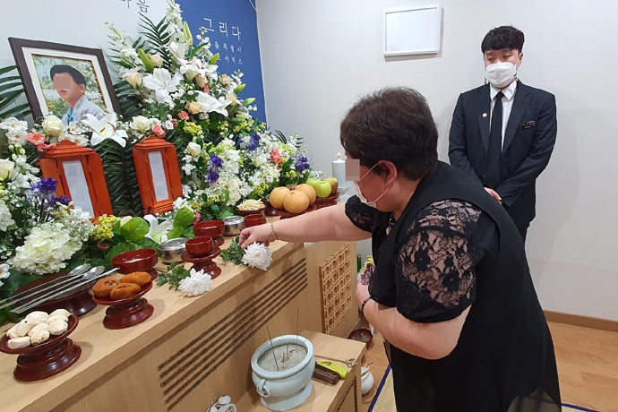 고립사한 동생의 장례에 참석한 누나가 의전업체 집례자의 안내를 받고 제단에 꽃을 올리고 있다. 사진 나눔과나눔