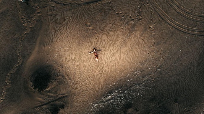 무엇으로 만나든 담담히. 사막 한가운데 한 사람이 팔을 벌리고 누워 있다. 바닥에는 발자국, 바퀴 자국이 나 있다. 사진 언스플래시