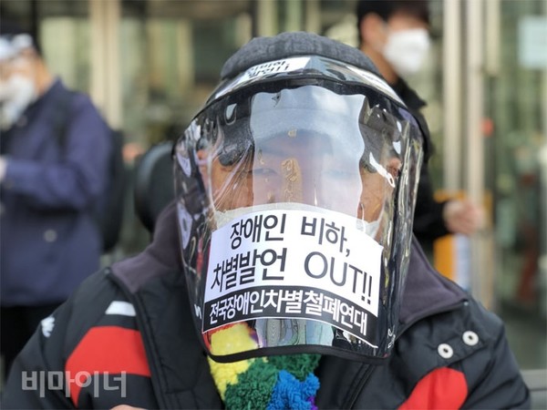 기자회견에 참가한 한 장애인이 코로나19 방지를 위해 비닐로 된 캡모자를 얼굴 아래까지 내려썼다. 비닐로 된 캡모자에는 “장애인 비하, 차별 발언 아웃(OUT)”이라는 문구가 쓰여 있다. 사진 강혜민