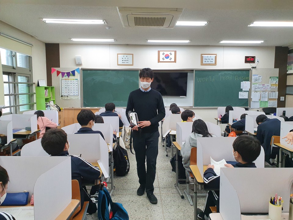 교실 안에서 김헌용 교사가 등교한 학생들 사이에서 마스크를 끼고 수업하고 있다. 그의 손에는 점자정보단말기가 들려 있다. ⓒ김헌용