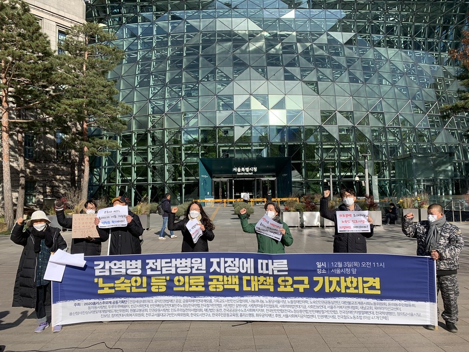 시민 사회 단체는 서울시청 앞에서 기자회견을 열었다. 참가자 7명이 주먹을 쥐고 하늘을 향해 뻗으며 결의를 다지고 있다. 현수막에는 '감염병 전담 병원 지정에 따른 '노숙인 등' 의료 공백 대책 요구 기자회견'이라고 적혀 있다. ⓒ빈곤사회연대